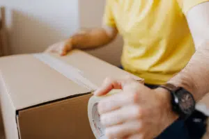 Man in yellow tshirt sealing up a box with packing tape.