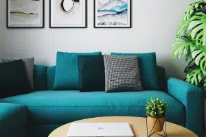 Green couch sitting in living room with beige wood table in front of it and three pictures hanging above it.