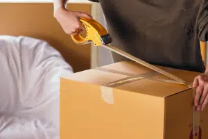 A woman taping the top of a medium sized cardboard box.