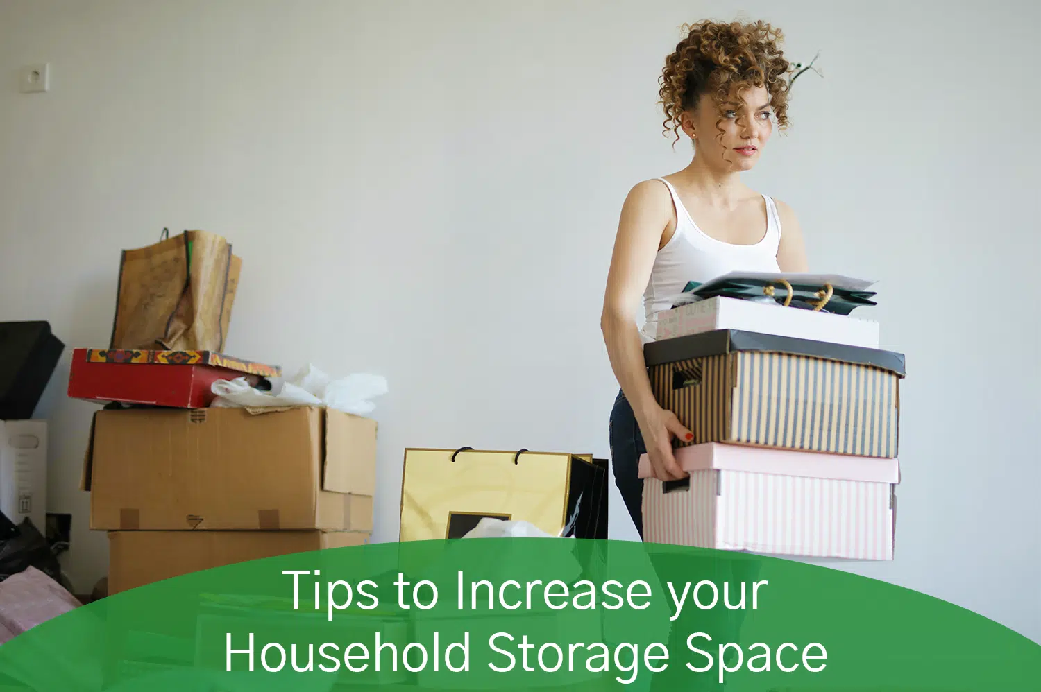 A white woman with curly brown hair carying four boxes with extra boxes and things behind her.