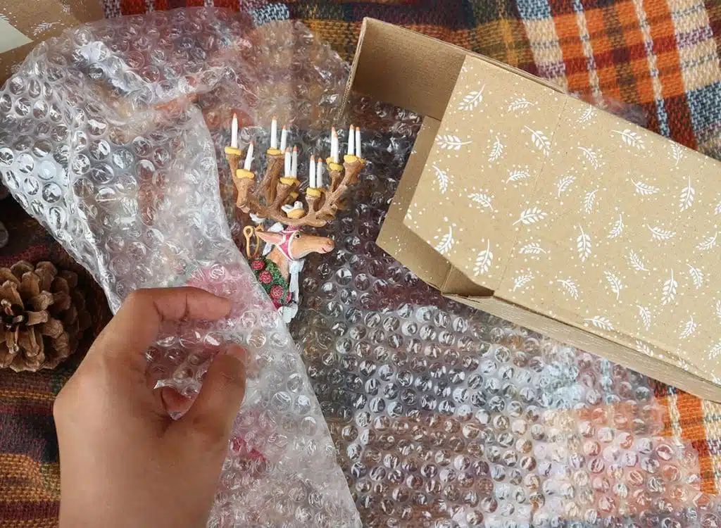 A hand wrapping a fragile holiday ornament in bubble wrap